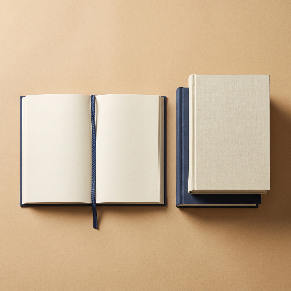A stack of plain books, one open, on a sand-colored surface