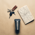 Car keys, a folded map and a travel cup on a sand-colored surface