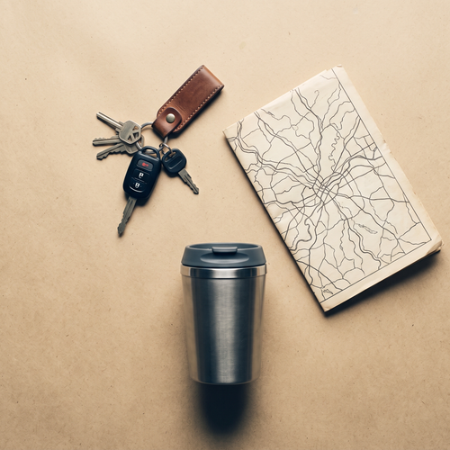 Car keys, a folded map and a travel cup on a sand-colored surface