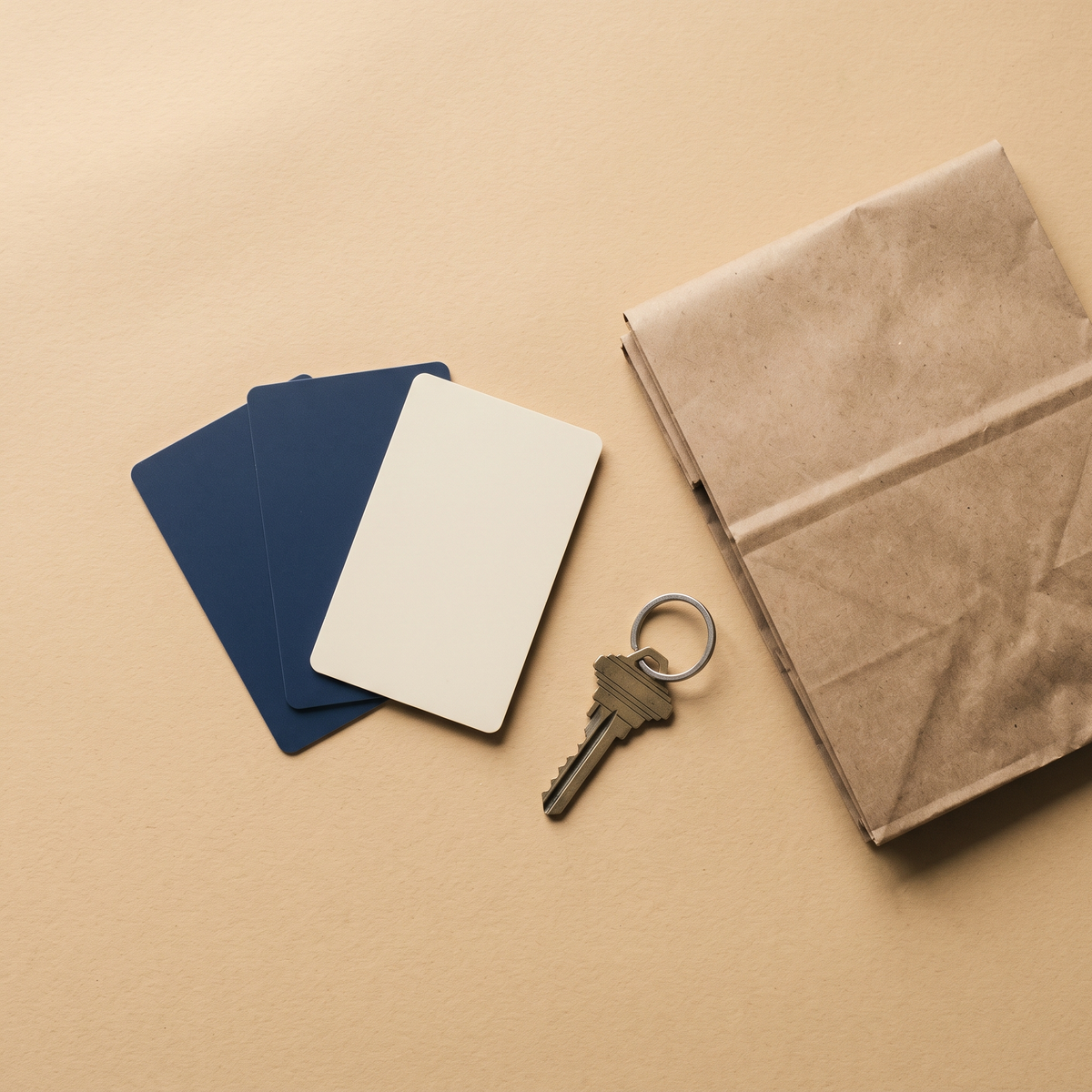 Blank gift cards, a folded paper grocery bag and a house key on a sand-colored surface